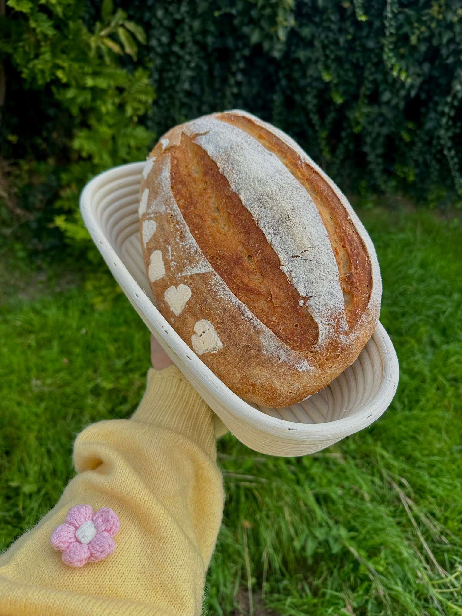 Een goudbruin wit zuurdesembrood met bloemhartjes op de korst, in een rieten rijsmand