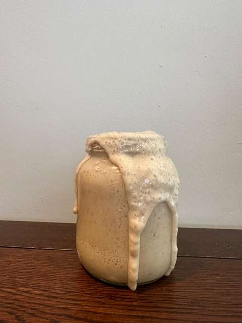 Een bruisende zuurdesemstarter die over de rand van een glazen pot borrelt